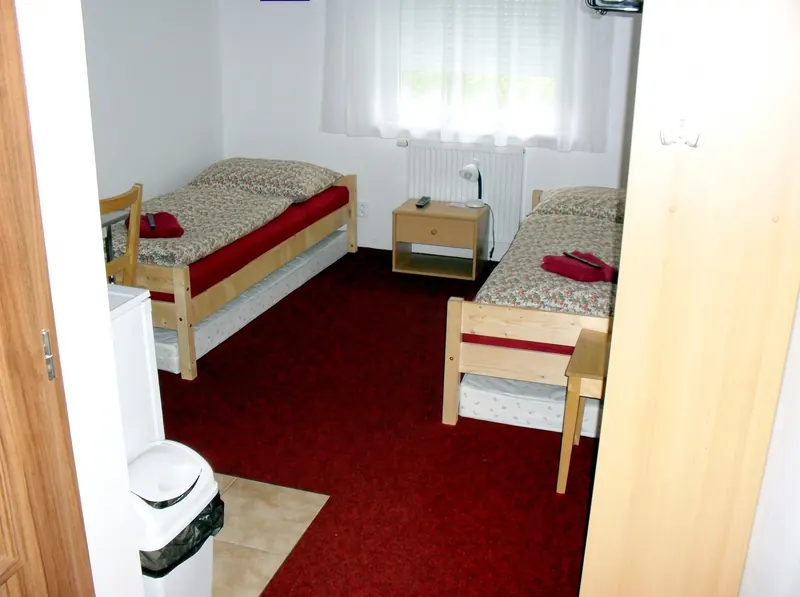 Dvoulůžkový pokoj se dvěma postelemi, nočním stolkem a oknem