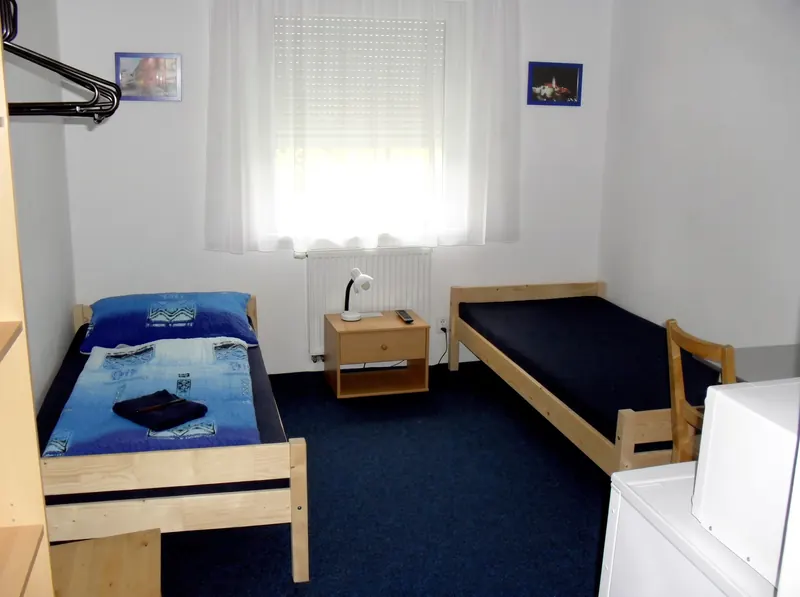 Pokoj se dvěma postelemi, modrým kobercem a oknem se záclonou