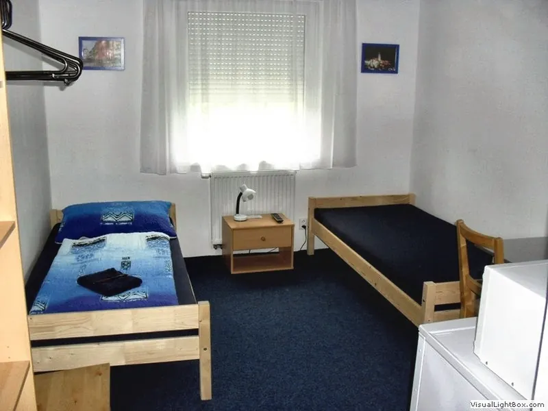 Pokoj se dvěma postelemi, modrým kobercem a oknem se záclonou