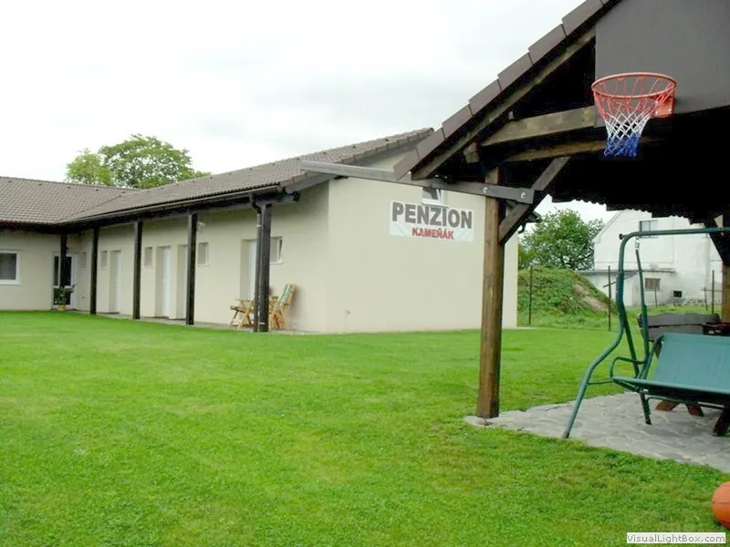 Přízemní budova penzionu Kameňák s řadou vchodů do pokojů, trávník a dřevěná pergola