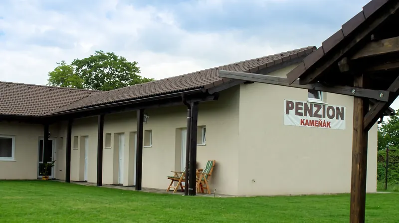 Přízemní budova penzionu Kameňák s cedulí, řadou vchodů do pokojů a trávníkem