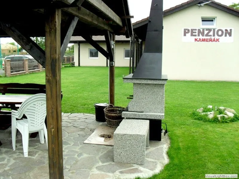 Venkovní krb s grilem pod pergolou a posezení na trávníku